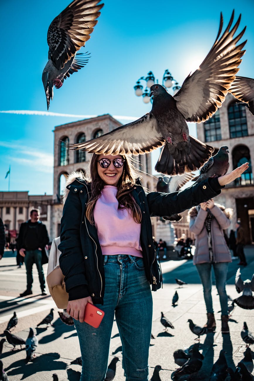 woman smiles and stands near flying pigeons